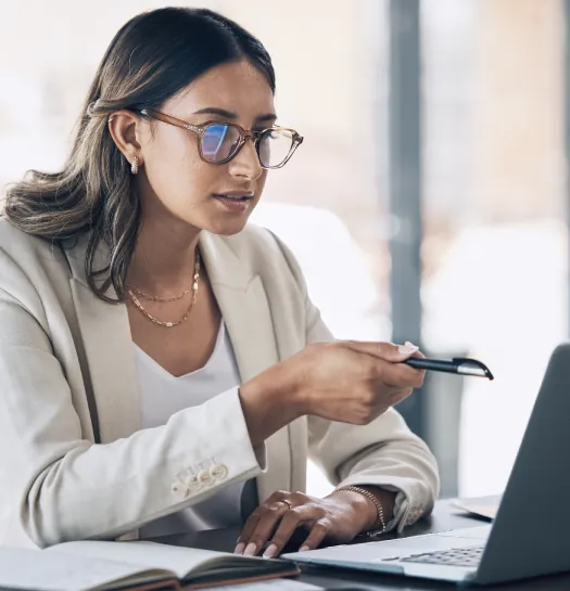 A woman wearing glasses is focused on her laptop screen, engaged in work or research.